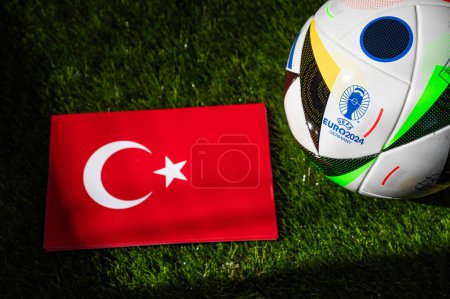Foto de HAMBURG, ALEMANIA, 17 DE ABRIL DE 2024: Bandera nacional de Turquía y balón de fútbol oficial del torneo de fútbol Euro 2024 en Alemania colocado sobre hierba verde. Fondo negro, editar espacio - Imagen libre de derechos