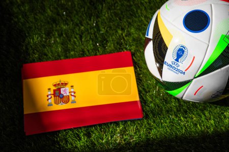 Photo for LEIPZIG, GERMANY, APRIL 17, 2024: Spain national flag and official soccer ball of Euro 2024 football tournament in Germany placed on green grass. Black background, edit space - Royalty Free Image