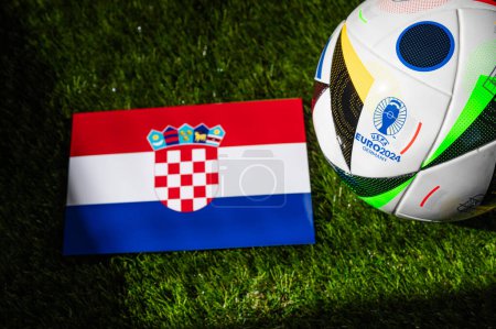 LEIPZIG, DEUTSCHLAND, 17. April 2024: Kroatiens Nationalflagge und offizieller Fußball-Ball der Fußball-EM 2024 in Deutschland auf grünem Rasen platziert. Schwarzer Hintergrund, Raum bearbeiten