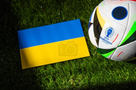 Foto de LEIPZIG, ALEMANIA, 17 DE ABRIL DE 2024: Bandera nacional de Ucrania y balón de fútbol oficial del torneo de fútbol Euro 2024 en Alemania colocado sobre hierba verde. Fondo negro, editar espacio - Imagen libre de derechos