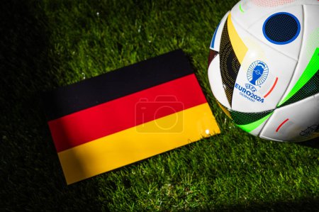 Foto de BERLÍN, ALEMANIA, 17 DE ABRIL DE 2024: Bandera nacional de Alemania y balón de fútbol oficial del torneo de fútbol Euro 2024 en Alemania colocado sobre hierba verde. Fondo negro, editar espacio - Imagen libre de derechos