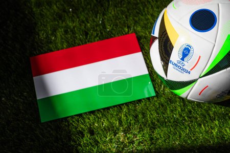 Téléchargez les photos : LEIPZIG, ALLEMAGNE, 17 AVRIL 2024 : Drapeau national hongrois et ballon de football officiel du tournoi de football Euro 2024 en Allemagne placé sur l'herbe verte. Arrière-plan noir, modifier l'espace - en image libre de droit