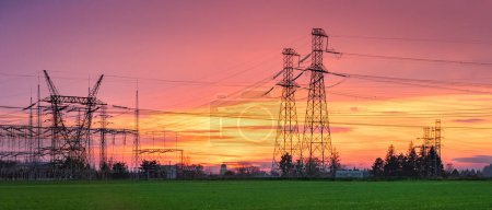 Foto de Líneas de alto voltaje con mástiles altos en el campo, cielo colorido en tonos rosados anaranjados después de la puesta del sol. - Imagen libre de derechos