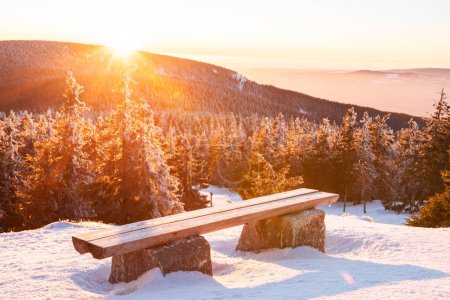 Sudetes, a bench with a view of the mountain landscape at sunset, a view from the hiking trail in winter.