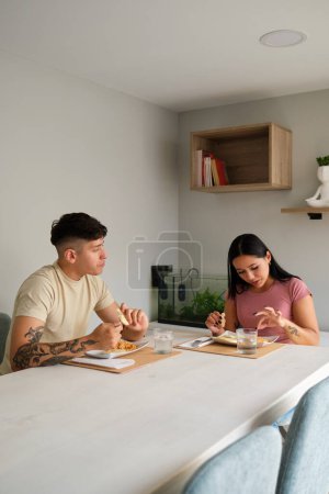 Foto de Dos jóvenes hispanos comiendo arepas tradicionales en la sala de estar. - Imagen libre de derechos