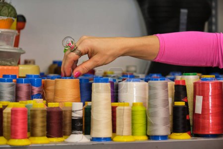 Photo for Unrecognizable dressmaker with colorfull clothes choosing a thread in a sewing workshop. - Royalty Free Image