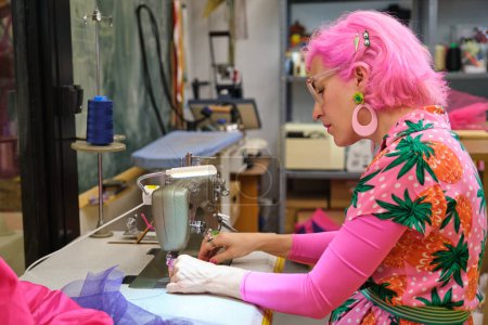 Photo for Tailor with pink hair and colorfull clothes threading sewing machine in a sewing workshop. - Royalty Free Image
