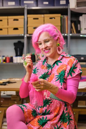 Photo for Dressmaker with pink hair and colorfull clothes hand sewing a piece of fabric in a sewing workshop. - Royalty Free Image