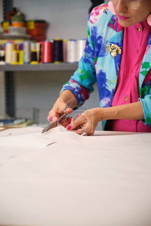 Photo for Dressmaker with colorfull clothes cutting sewing patterns in a sewing workshop. - Royalty Free Image