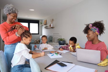 Foto de African family having a snack while painting or doing the homework. Horizontal extended family spending time together. - Imagen libre de derechos