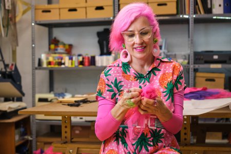 Photo for Seamstress with pink hair and colorfull clothes hand sewing a piece of fabric in a sewing workshop. - Royalty Free Image