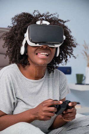 Foto de Joven mujer negra juega videojuegos con auriculares VR en la cama por la mañana. - Imagen libre de derechos