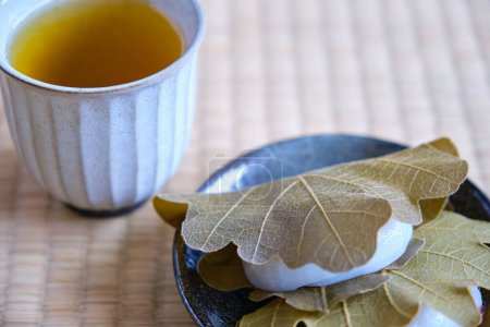 Photo for Kashiwa mochi and green tea on tatami. Japanese mochi with anko filling wrapped with an oak leaf. Japanese sweets. - Royalty Free Image