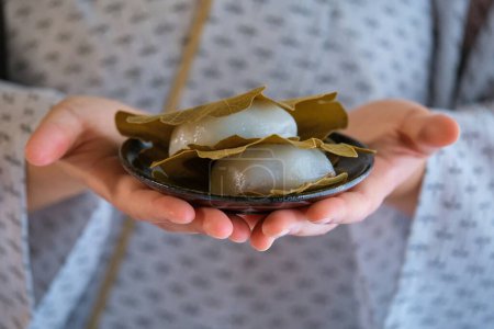 Photo for Hands holding japanese Kashiwa mochi. Japanese mochi with red bean paste filling wrapped with an oak leaf. Japanese sweets. - Royalty Free Image