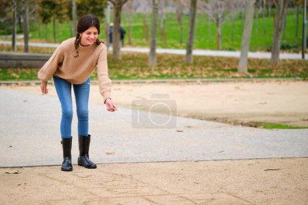 Photo for Girl with two braids playing hopscotch drawn in the sand outdoors. - Royalty Free Image