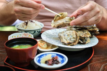 Téléchargez les photos : Touriste européen méconnaissable mangeant des huîtres traditionnelles à Miyajima, Hiroshima, Japon. - en image libre de droit