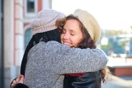 Photo for Two multiracial female happy friends hugging each other and smiling on city street. - Royalty Free Image