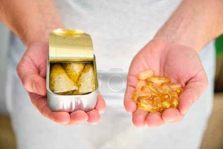 A person is holding a can of sardines in one hand and omega 3 fish oil capsules in the other.