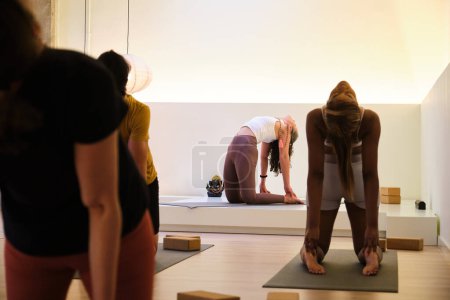 A group of people are practicing ustrasana or camel yoga pose in a room. Yoga class.