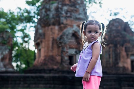 Photo for A young Southeast Asian girl walks to study the history of the ancient Khmer castle Khu Suan Taeng in Thailand, Buriram. - Royalty Free Image