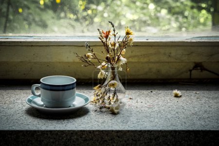 Téléchargez les photos : Un bâton de fenêtre morbide avec tasse à café et fleurs flétries dans un endroit perdu - en image libre de droit