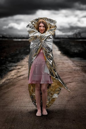 a fantasy woman is standing on a road wearing a silver and gold rescue blanket