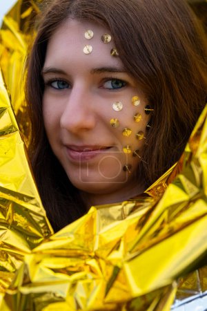 a woman as a fantasy representation with tacks in her face and a golden rescue blanket