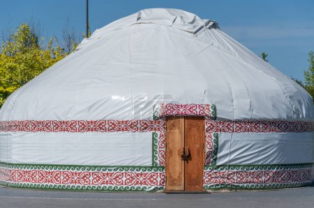 Téléchargez les photos : Yourte blanche ronde kazakhstan nomades. Maison traditionnelle asiatique avec ornement et porte. Demeure mongolienne, kyrgyzstan, Ouzbékistan des tribus. Maison nationale Est. Camp de vacances extérieur. Mode de vie nomades. - en image libre de droit