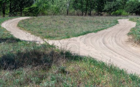 Sand road in the forest. Track imprint of quadricycle on nature land. Tire pattern of quad bike on driveway. Sand texture off road. Path in forest close up. Sand mounds and green plants in sunny day.