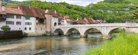 Téléchargez les photos : Paysage urbain avec pont traversant la rivière Doubs dans le village pittoresque Saint-Ursanne dans le canton du Jura quartier Porrentruy en Suisse - en image libre de droit