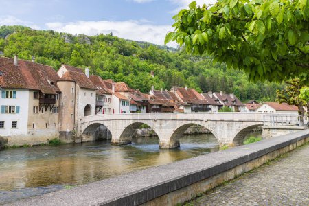 Téléchargez les photos : Paysage urbain avec pont traversant la rivière Doubs dans le village pittoresque Saint-Ursanne dans le canton du Jura quartier Porrentruy en Suisse - en image libre de droit