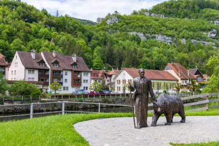 Téléchargez les photos : St-Ursanne, Suisse - 15 mai 2023 : homme avec sculpture d'ours le long de la rivière Doubs dans le village pittoresque Saint-Ursanne dans le canton du Jura quartier Porrentruy en Suisse - en image libre de droit