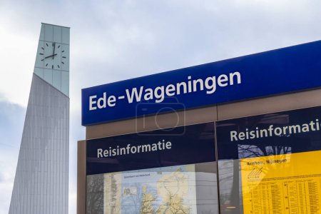 Téléchargez les photos : Ede, Pays-Bas - 1er mars 2024 : Panneau d'information avec tour d'horloge en arrière-plan à la nouvelle gare centrale d'Ede-Wageningen qui a été développée sur la base des principes de durabilité. - en image libre de droit