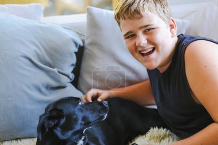 Photo for Teen boy snuggling on couch with pet dog. Man's best friend. Black kelpie cross labrador breed. - Royalty Free Image