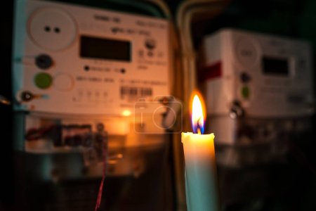 Stromzähler, der durch das Licht einer brennenden Kerze beleuchtet wird. Stromausfall, Energiekrise oder Blackout-Konzept.