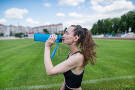Photo for The sportswoman drinks water at the stadium. Outdoor workout. - Royalty Free Image