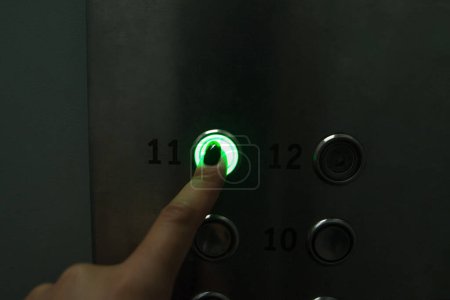 Téléchargez les photos : Une main appuie sur un bouton rond dans un ascenseur dans le noir. La femme va au 11ème étage. - en image libre de droit
