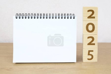 2025 ist die Zeit für einen Neuanfang. 2025 aus Würfeln und blankem Notizbuch auf Holztisch. Neujahr. Schreibtischkalender 2025 für Planer und Erinnerungsorganisator.