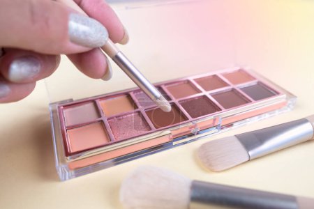 Close up a palette with colorful eye shadows and a makeup brush. Decorative women's cosmetics. Make-up artist. Close up makeup artist uses a brush to pick up eyeshadow from the palette