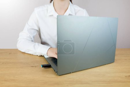 Erntefoto einer jungen Geschäftsfrau, die vor einem grauen Wandhintergrund posiert und mit einem Laptop auf einem Stuhl sitzt.
