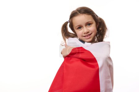 Foto de Retrato aislado sobre fondo blanco de una hermosa niña, envuelta orgullosamente en la bandera de Polonia o Canadá. Concepto de fiestas nacionales y eventos patrióticos. Patriotismo. Día de la Independencia - Imagen libre de derechos