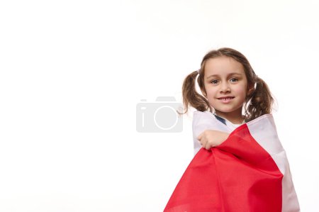 Foto de Niña europea, envuelta orgullosamente en la bandera de Polonia o Canadá, aislada sobre fondo blanco. Concepto de fiestas nacionales. Eventos patrióticos. Ciudadanía. Patriotismo. Día de la Independencia. Espacio publicitario - Imagen libre de derechos