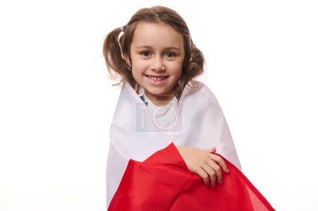 Foto de Pequeño ciudadano polaco europeo, un niño encantador, niña envolviendo la bandera de Polonia, celebra el Día de la Independencia el 11 de noviembre, aislado sobre fondo blanco con espacio para copiar texto promocional - Imagen libre de derechos