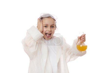 Téléchargez les photos : Petite fille excitée, écolière, jeune chimiste scientifique en blouse blanche, effectuant une expérience scientifique ou une réaction chimique au laboratoire de chimie, isolée sur fond blanc - en image libre de droit