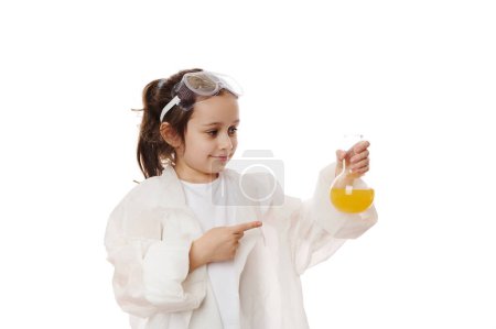 Téléchargez les photos : Petite fille intelligente, étudiante pointant du doigt une fiole avec un liquide chimique jaune, faisant des expériences scientifiques en classe de chimie pratique. Jeune chimiste scientifique isolé sur fond blanc. Copier l'espace publicitaire - en image libre de droit