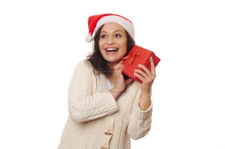 Téléchargez les photos : Adorable femme du Moyen-Orient au chapeau de Père Noël, en prévision des vacances d'hiver, excitée par le cadeau, isolée sur fond blanc avec espace publicitaire à copier. Il est temps d'ouvrir les cadeaux de Noël. atmosphère de Noël - en image libre de droit