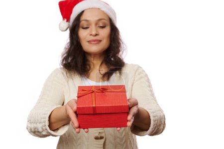 Téléchargez les photos : Focus sélectif sur une belle boîte cadeau rouge avec surprise à l'intérieur, entre les mains d'une jolie femme au chapeau de Père Noël remettant le cadeau de Noël heureux sur la caméra, isolé sur fond blanc. Jour de boxe - en image libre de droit