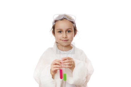Téléchargez les photos : Jolie petite fille, petite chimiste-scientifique tenant des éprouvettes avec des produits chimiques liquides, souriante regardant la caméra, isolée sur fond blanc. Développement précoce des enfants. Chimie. Copier l'espace publicitaire - en image libre de droit
