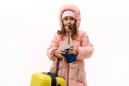 Téléchargez les photos : Beautiful Caucasian little girl in pink down coat, going for vacations, looking at camera, posing with suitcase and boarding pass on white background with free advertising space. Travel Trip Journey - en image libre de droit