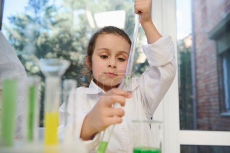 Téléchargez les photos : Smart little girl, primary school student using graduated pipette, dripping reagent into a test tube, while a chemical experiments, at chemistry class. Back to school on new semester of academic year - en image libre de droit